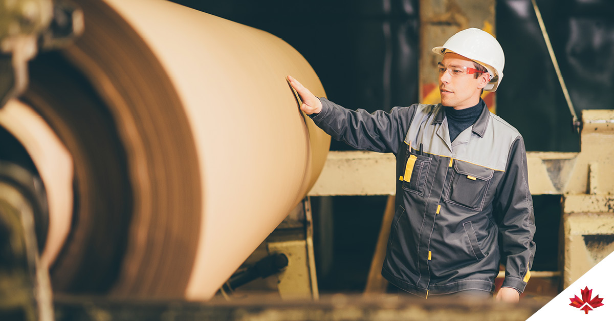 Un employé de l’usine de papier est posté près d’une machine à papier kraft et porte un équipement de protection.    