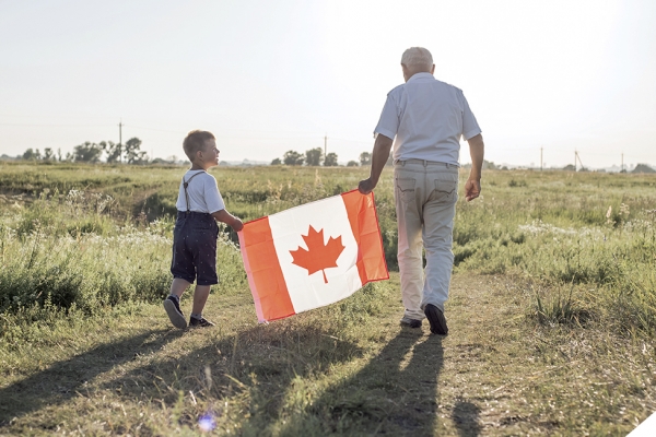 child and elderly man walking in field holding a Canada flag