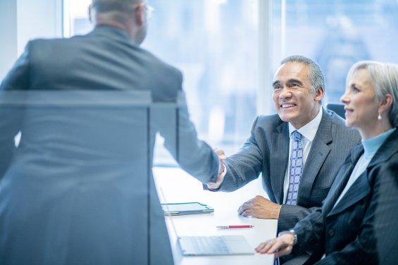 Mains d’hommes d’affaires asiatiques et afro-américains mûrs se serrant la main dans un bureau lumineux lors d’une réunion, vêtus de costumes.