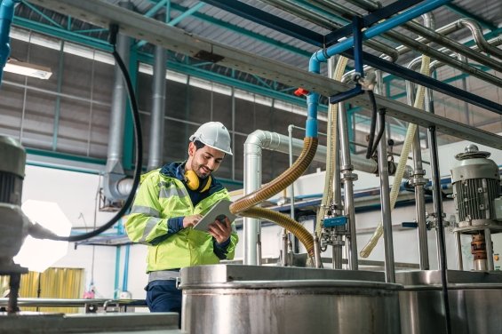 Technicien ingénieur caucasien en uniforme avec une tablette vérifiant et contrôlant des réservoirs et des conduites de liquide dans une ligne de production d’usine chimique.