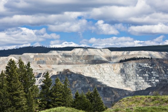 Site minier à ciel ouvert dans les Rocheuses canadiennes, en Colombie-Britannique, montrant des terrasses de terre et la forêt environnante.