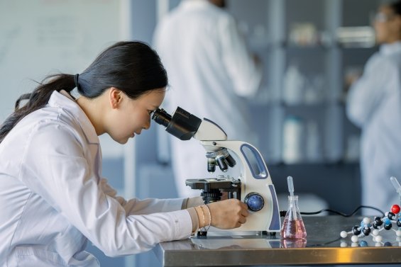 Technicien de laboratoire examinant un échantillon liquide dans un flacon, portant des gants bleus, avec du matériel scientifique en arrière-plan.
