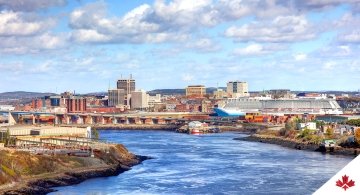 Paysage de Saint John (Nouveau-Brunswick), y compris des immeubles de bureaux et des immeubles commerciaux, l’infrastructure de transport, un plan d’eau et des petits et grands bateaux.