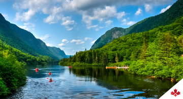Végétation luxuriante, voie navigable et ciel au-dessus de la rivière Jacques-Cartier au Québec, Canada avec kayakistes sur l’eau.