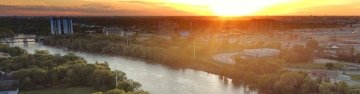 Vue aérienne de Winnipeg, Manitoba, Canada, au coucher du soleil, avec une rivière traversant la ville et un pont au premier plan. 