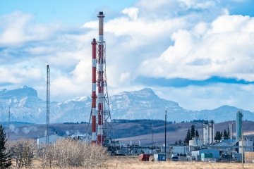 Usine pétrolière et gazière avec de hautes torchères surplombant les Rocheuses canadiennes près de Cochrane, Alberta, Canada.