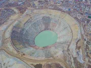 Une grande mine de diamants à ciel ouvert, circulaire et en gradins, vue du dessus, avec un bassin vert‑bleu au centre.