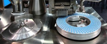 Gros plan de capsules bleues disposées en motif circulaire sur une machine métallique dans une ligne de production pharmaceutique.