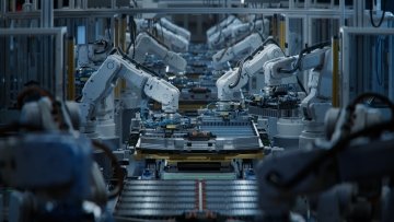Des bras robotiques blancs alignés le long d’une chaîne de production automatisée, assemblant des composants de batteries pour véhicules électriques.