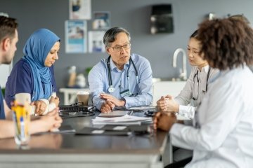 Un groupe diversifié de professionnels de la santé en discussion, favorisant le travail d’équipe et la collaboration dans un environnement hospitalier.