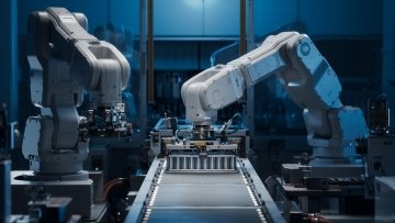 Des bras robotiques blancs assemblent des composants de batteries pour véhicules électriques sur une ligne de production automatisée dans une usine moderne.