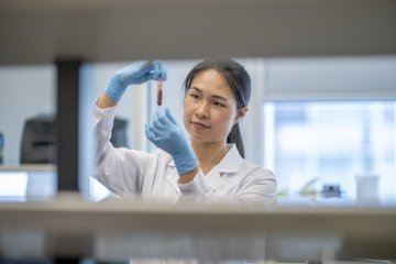 Une technicienne de laboratoire d’origine asiatique examine de près un flacon de sang avant de le placer dans la centrifugeuse pour traitement.