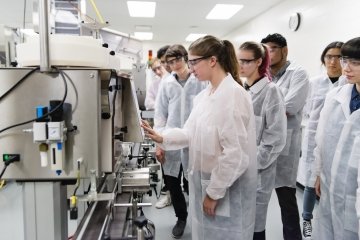 Groupe multiethnique de nouveaux étudiants collégiaux découvrant l’équipement de laboratoire pharmaceutique. Grand groupe de personnes portant des équipements de protection, des lunettes et des blouses de laboratoire.
