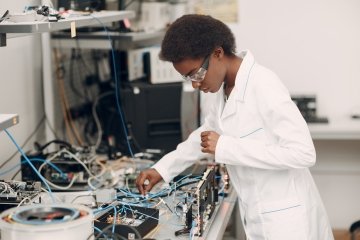 Une scientifique afro-américaine travaille à une paillasse de laboratoire avec des instruments électroniques, notamment des fils, des outils et un microscope.