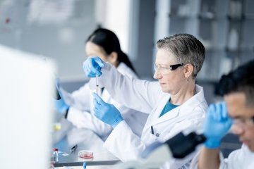 Trois techniciens de laboratoire travaillent ensemble dans un laboratoire scientifique pour mener diverses expériences et consigner leurs résultats. Ils portent tous des blouses blanches, des gants et des lunettes de protection.