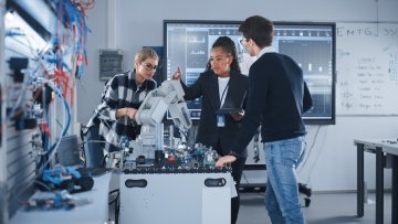 Enseignante et étudiants travaillant ensemble dans un laboratoire de robotique avec de l’équipement électronique.