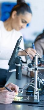 Gros plan de mains travaillant sur des circuits imprimés et des composants électroniques.