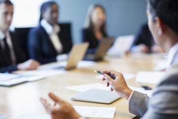 Mains d’un homme d’affaires gesticulant lors d’une réunion, un stylo à la main, illustrant le leadership et la prise de décision autour d’une table de conférence.