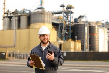 Ingénieur tenant un talkie-walkie VHF et des notes, usine en arrière-plan. Homme portant un casque et une combinaison de travail. Concept du métier d’ingénieur et des technologies modernes.